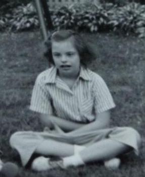 Girl with short hair sitting cross legged on ground outside