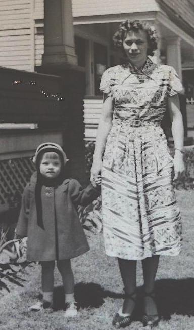 Woman with curly hair holding hands with child in peacoat with Down Syndrome in late 1940s